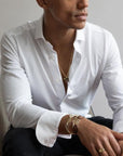 Man draagt witte blouse en Amsterdam bracelet gold armband van Odile zittend op stoel