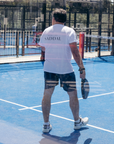Man speelt padel in YVES ODILE sportkleding met witte shirt en zwarte shorts op blauw veld