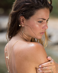 Odile gold rings on woman's fingers paired with matching gold earrings and layered necklaces outdoor