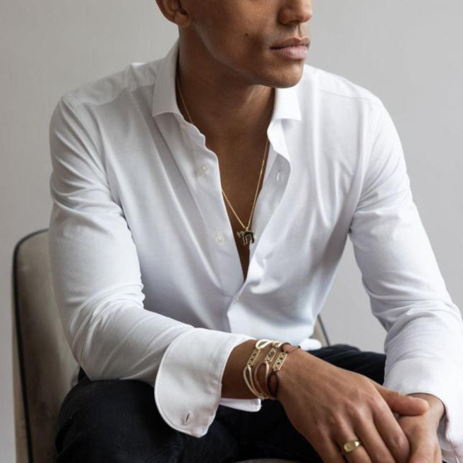 Man draagt witte blouse en Amsterdam bracelet gold armband van Odile zittend op stoel