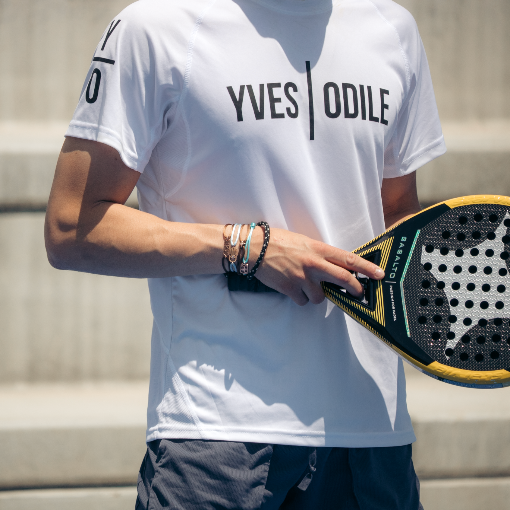Man draagt witte YVES ODILE sportkleding t-shirt tijdens padelspel met zwart gele padelracket